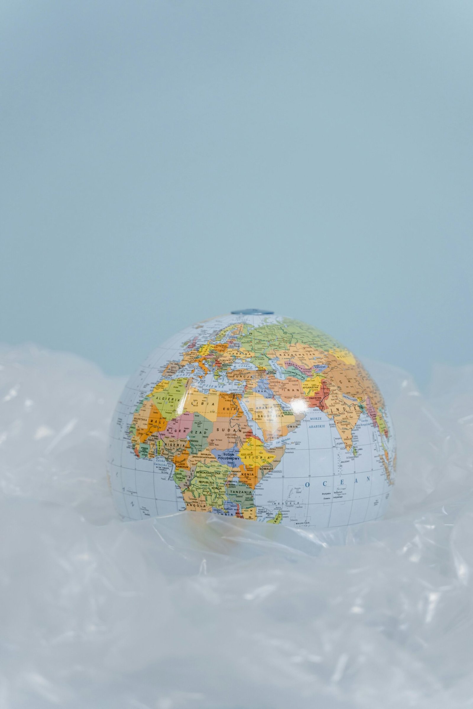 A globe surrounded by plastic against a soft blue background, symbolizing environmental issues.